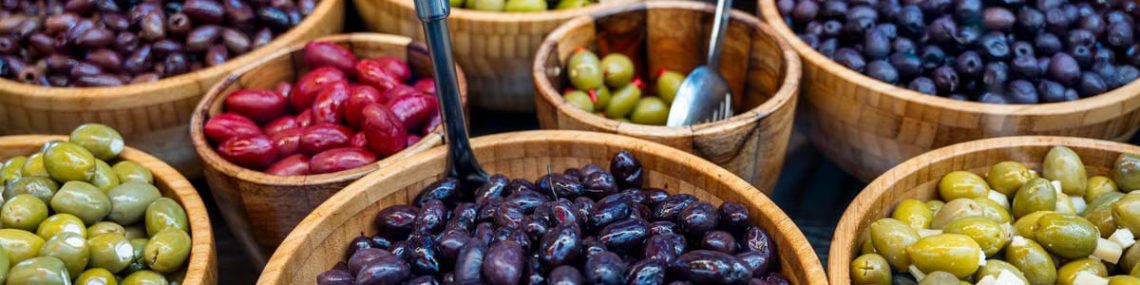 Various types of olives displayed in wooden bowls at an outdoor market.