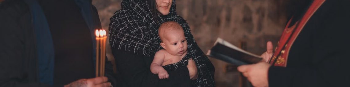 A touching moment during an Orthodox baptism ceremony with a priest, parents, and baby.
